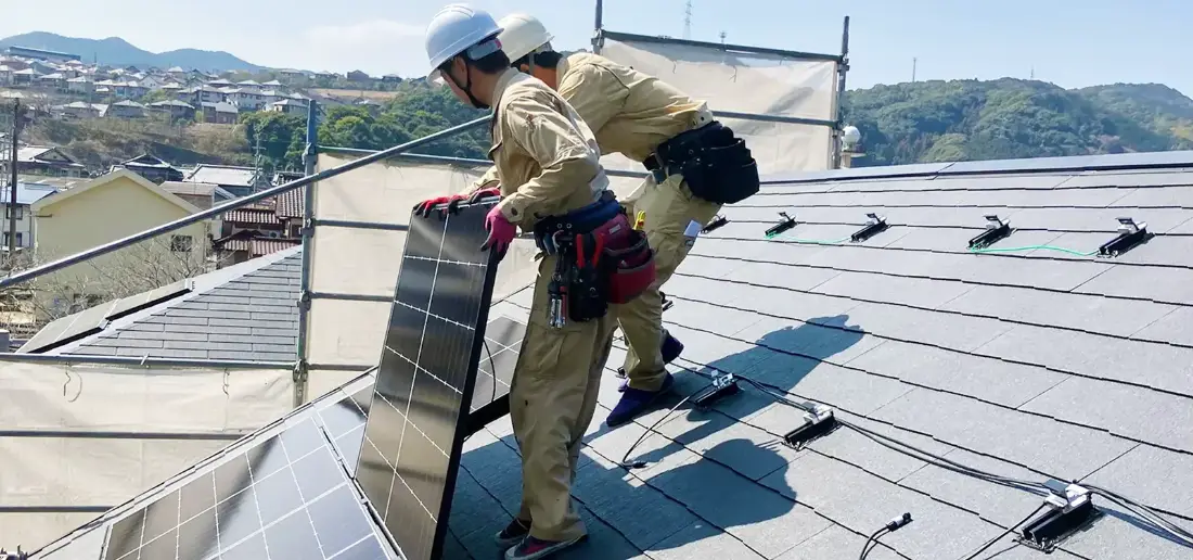 屋根の上で太陽光パネルを運ぶ施工スタッフ