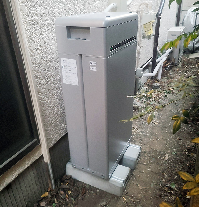 Outdoor air conditioning/heat pump condenser cabinet on a concrete pad beside a stucco wall, with pipes and wiring nearby.
