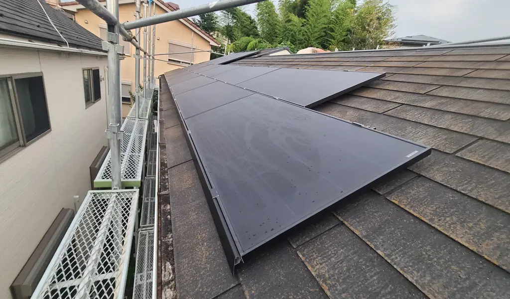 町田市のスレート屋根の軒側に並べた太陽光パネルと工事用の足場