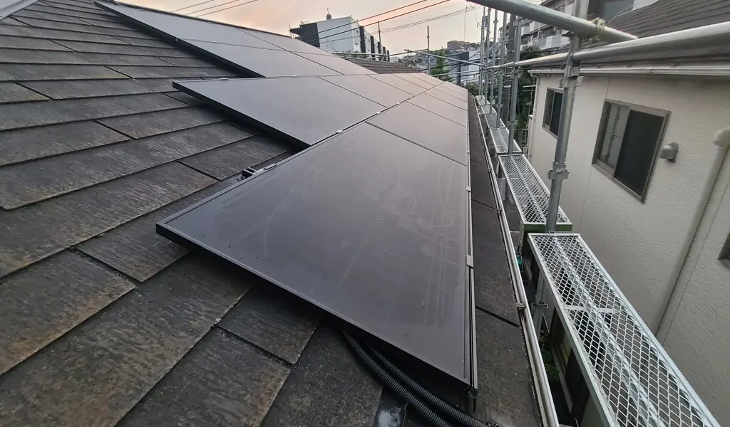 町田市のスレート屋根に段違いに並べた太陽光パネルと配線の管